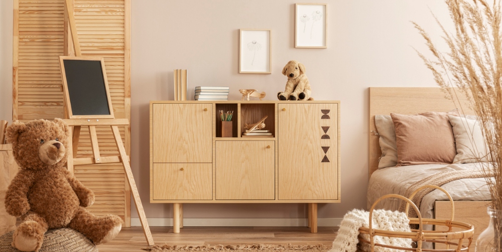 Teddy bear on pouf and small blackboard on easel in stylish kid's bedroom
